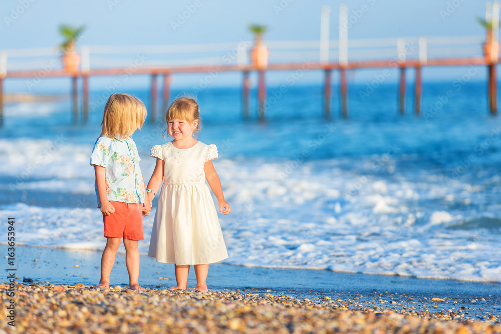 Couple of happy elegant dressed boy and girl are walking along seashore and holding hands.