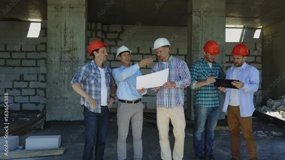 Aerial Shot Of Builders Team On Construction Site Discussing Plan Of Project With Architect And Contractor Using Blueprint On Digital Tablet Aerial Shot Of Builders Team On Construction Site Discussing Plan Of Project With Architect And Contractor Using Blueprint On Digital Tablet