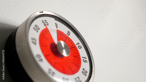 Classical vintage kitchen countdown timer close up shot with analog clock face and red remaining time display, 55 minutes left, low depth-of-field with blur