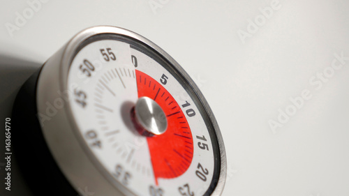 Classical vintage kitchen countdown timer close up shot with analog clock face and red remaining time display, 30 minutes left, low depth-of-field with blur