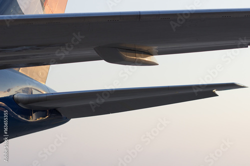 Tail wing of the aircraft in the light of the setting sun, view from under the main wing
