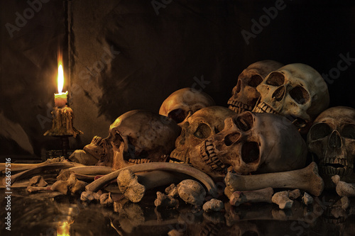 Pile of Skulls and bones on the reflection floor and old dirty wall have Lighting by candlelight photo