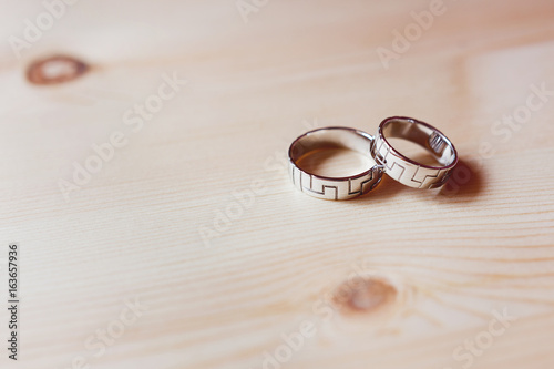 Pair of golden wedding rings with geometrical ornament on wooden background. Symbol of love, marriage and the fifth ("wooden") wedding anniversary.