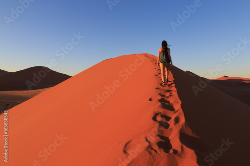Girl on sand dune in desert during sunrise.  Sossusvlei, Namib Naukluft National Park, Namibia
