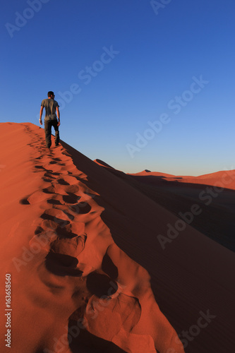 Man  on sand dune in desert during sunrise.  Sossusvlei  Namib Naukluft National Park  Namibia