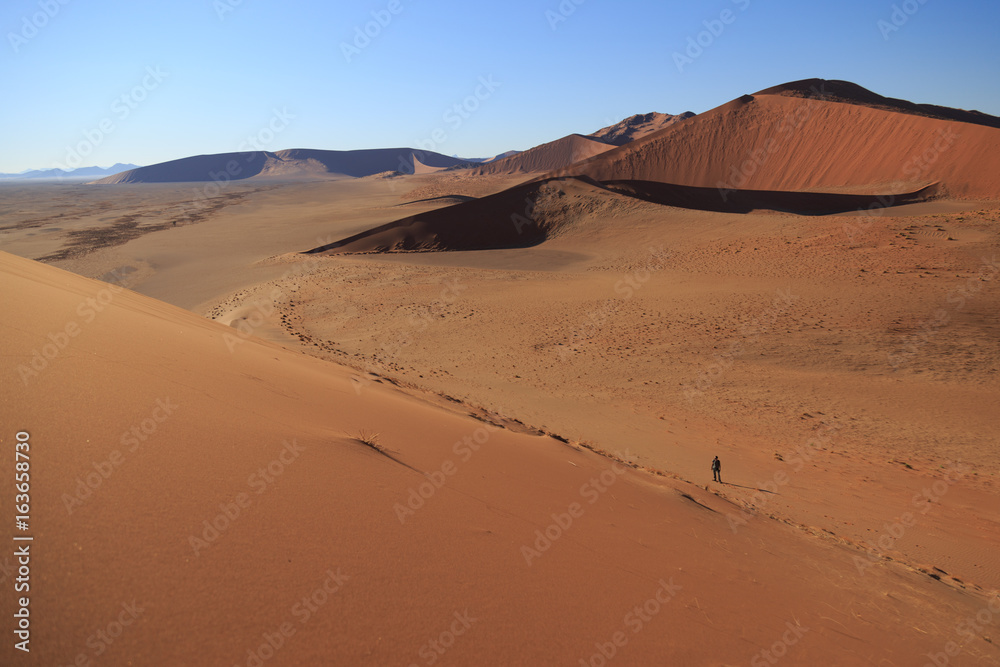 Man  on sand dune in desert during sunrise.  Sossusvlei, Namib Naukluft National Park, Namibia