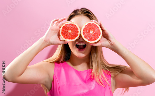 Happy young woman holding grapefruit halves on a pink background