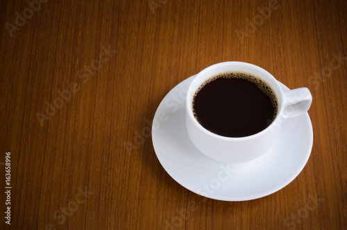 Black coffee in white ceramic cup on saucer over dark teak wood background with copy space for text insertion