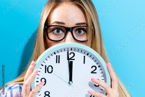 Young woman holding a clock showing nearly 12