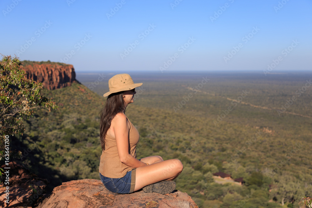 Naklejka premium Girl sitting on stone on the cliff at an forest landscape.