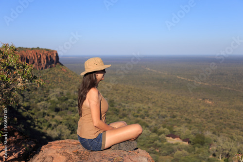 Girl sitting on stone on the cliff at an forest landscape.