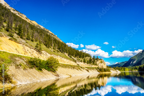 Reflections of blue sky, trees and mountains in the smooth surface on the crystal clear water of Crown Lake, along Highway 99 in Marble Canyon Provincial Park in British Columbia, Canada