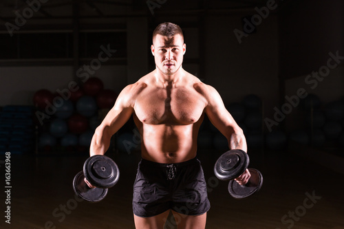 Muscular bodybuilder guy doing exercises with dumbbells.