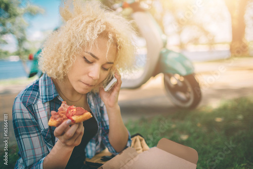 Girl Eating on moto scooter or moped. Girl Eating on moto scooter or moped. Happy Young woman holding hot pizza in box. Female student does not have time  he is going to eat on the go.