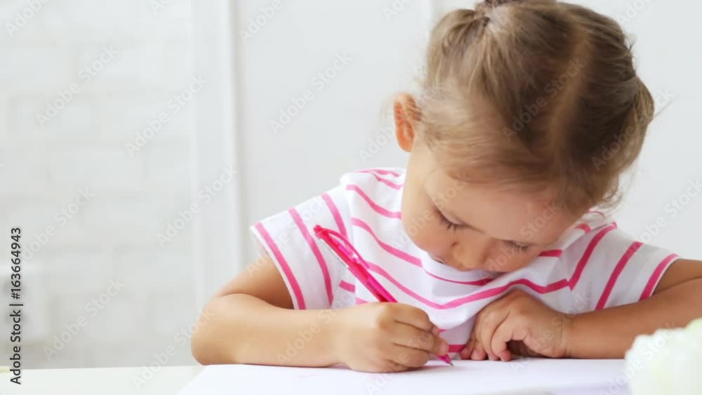 Cute preschool girl sitting by the white table focused on drawing something. Cute preschool girl sitting by the white table focused on drawing something.