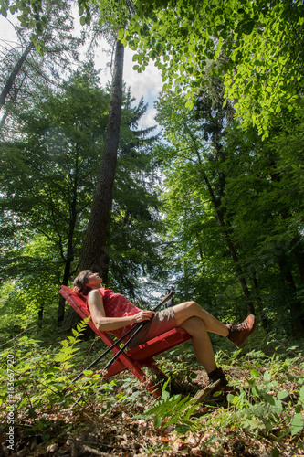 Frau sitzt mitten im Wald auf rotem Stuhl und entspannt sich von Wanderung