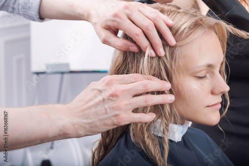 A hands of hairdresser making a haircut for a blonde girl