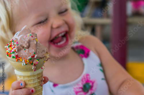 Laughing little blonde girl eating melting ice cream cone