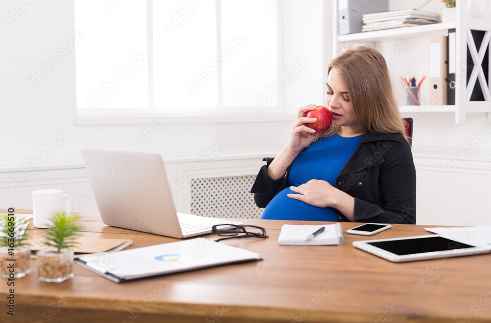 Pregnant woman eating apple in office copy space