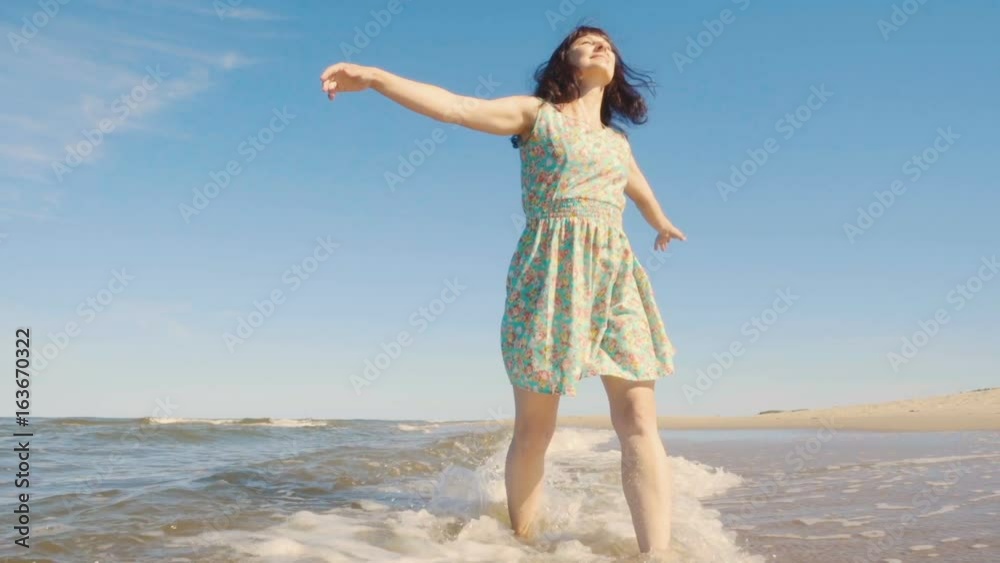 Attractive young woman in a dress strolls along the seacoast barefoot and enjoys herself. Beach with white sand. Outgoing coastal line. Slow Motion. Attractive young woman in a dress strolls along the seacoast barefoot and enjoys herself. Beach with white sand. Outgoing coastal line. Slow Motion.