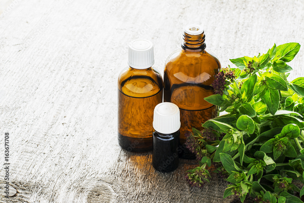 Essential oregano oil for aromatherapy in a dark glass containers on wooden background with fresh oregano. Selective focus. Essential oregano oil for aromatherapy in a dark glass containers on wooden background with fresh oregano. Selective focus.