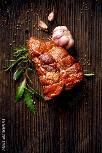 Smoked ham on a wooden rustic table with addition of fresh aromatic herbs and spices, natural product from organic farm, produced by traditional methods, top view