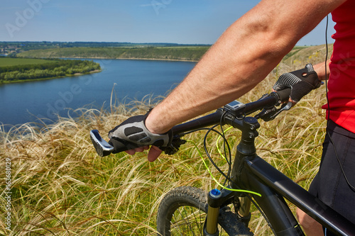 Close-up of the cyclist holding bicycle on the meadow in the countryside against beautiful landscape. photo