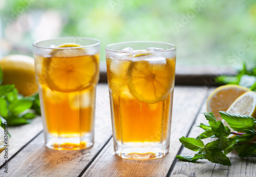 Ice tea with lemon slices on wooden table with a view to the terrace. Cold longdrink or lemonade. Close up summer vitamin antioxidant beverage. A frozen glass. Copy space for text.