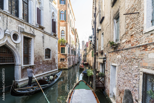 Facades of houses on a narrow canal with gondolas passing in Venice, Italy