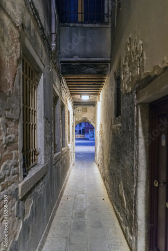 Very narrow cobblestone alley at night in Venice, Italy