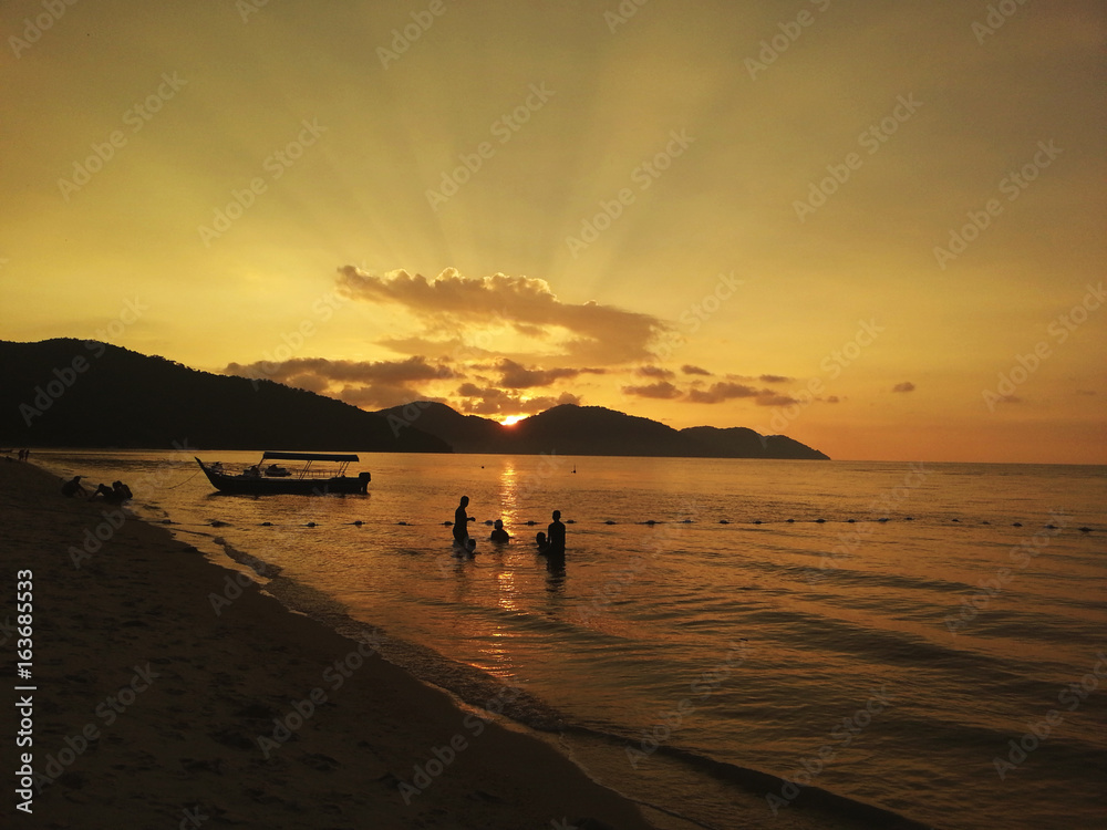 Breathtaking sunset view with sun rays over hills and silhouette of people enjoying the beach in tropical paradise of Penang island, Malaysia