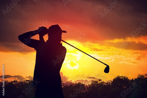 Silhouette of man playing golf at sunset.