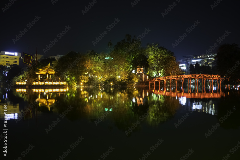 Night view of the Huc Bridge (Morning Sunlight Bridge) on the Hoan Kiem Lake (Lake of the Returned Sword) in historic centre of Hanoi, Vietnam. The bridge reflected in the lake.
