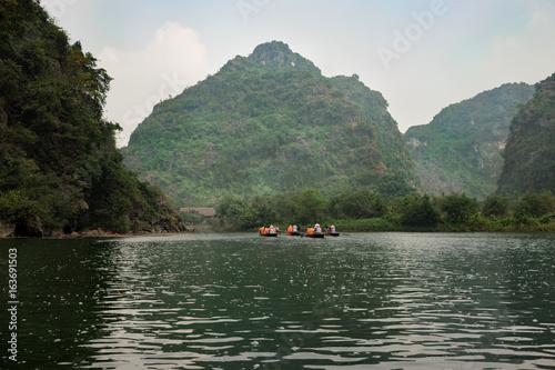 Tourists traveling in small boat along the River at the Trang An portion, Ninh Binh Province, Vietnam. Landscape formed by karst towers and plants along the river. Reed.