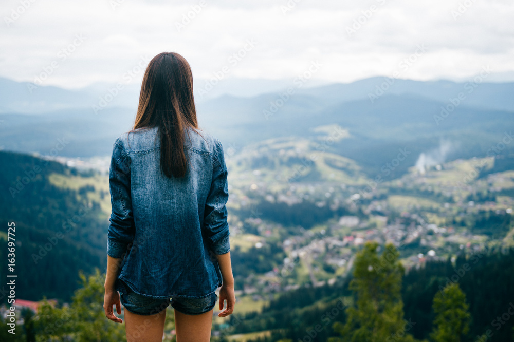 Lonely long legged skinny teenager pensive traveler girl in summer clothes standing on rocky stones at high top of carpathian mountain with cloudy sky. Dreaming and enjoying nature landscape. Vacation