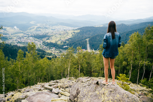 Lonely long legged skinny teenager pensive traveler girl in summer clothes standing on rocky stones at high top of carpathian mountain with cloudy sky. Dreaming and enjoying nature landscape. Vacation