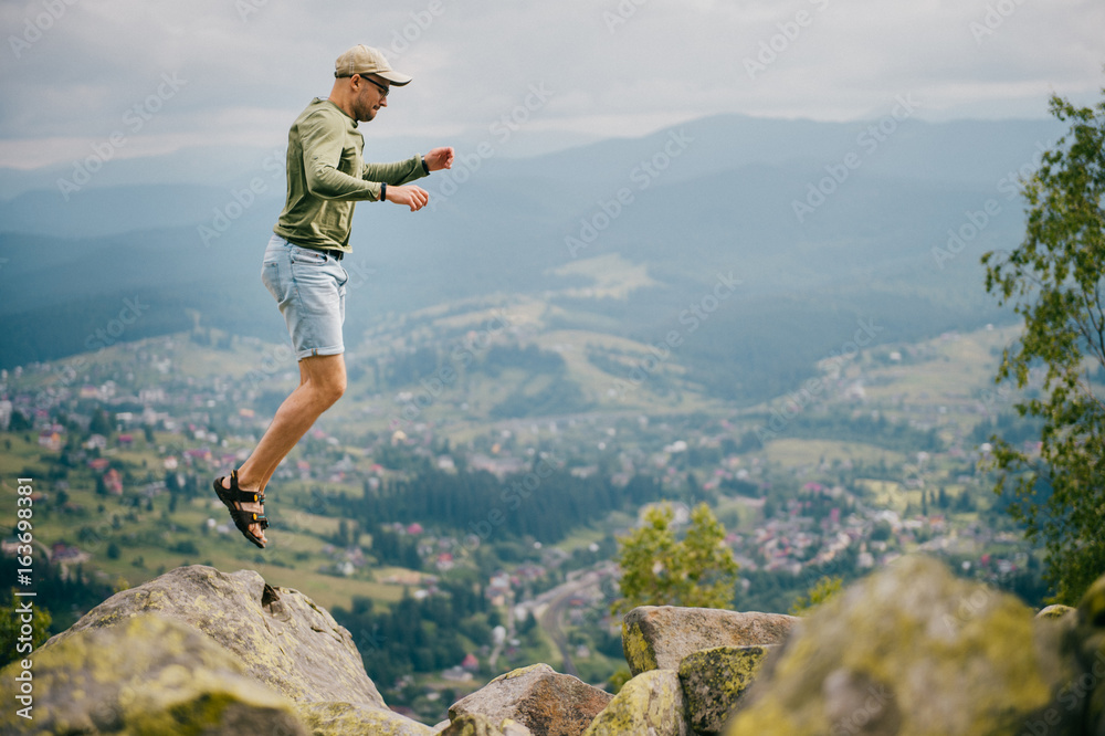 Traveler tourist sportsman in athletic footwear jumping from stone at top of mountain on high altitude outdoor. Greatness of nature landscape. Wellness, healthy lifestyle. Wild terrain in countryside.