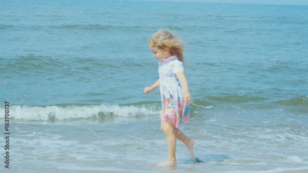 Adorable little girl in a dress runs jumping on the beach. Child enjoys playing on the seashore running on the water with pleasure. splashing in sea waves.Slow Motion Adorable little girl in a dress runs jumping on the beach. Child enjoys playing on the seashore running on the water with pleasure. splashing in sea waves.Slow Motion