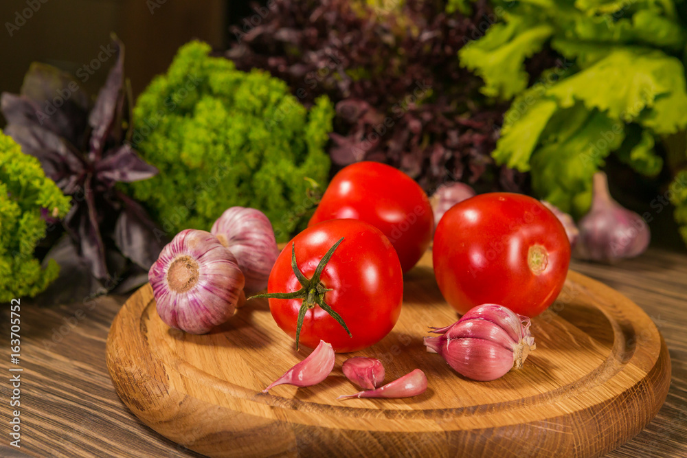 A wooden board with fresh tomatoes and garlic. Green salad in the background. A wooden board with fresh tomatoes and garlic. Green salad in the background.