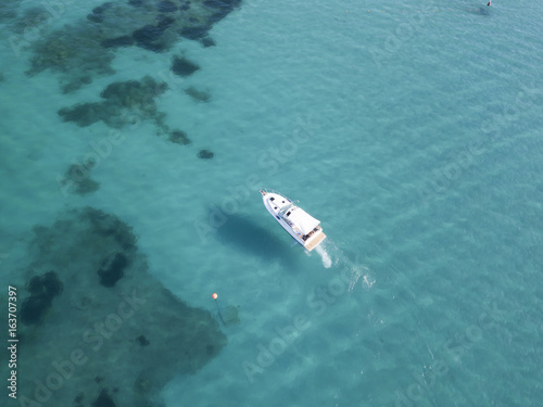 Aerial view of a little yacht on amazing beach with a turquoise and transparent sea. Emerald Coast, Sardinia, Italy.
