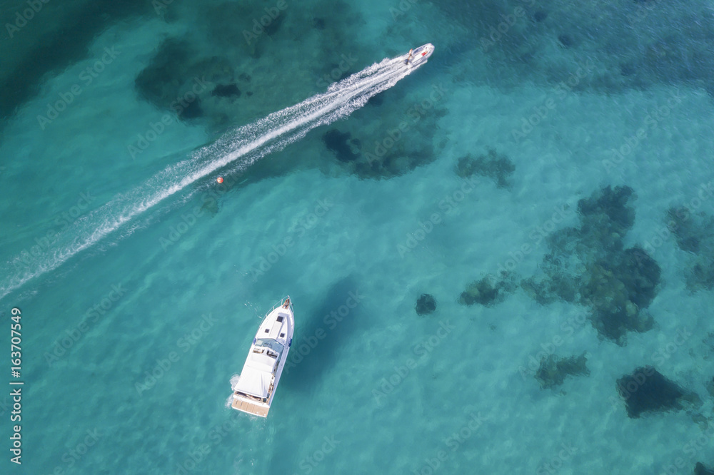 Aerial view of a little yacht on amazing beach with a turquoise and transparent sea. Emerald Coast, Sardinia, Italy.