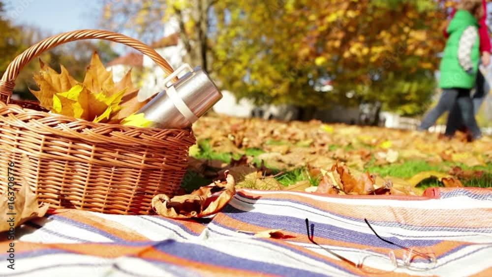 Father and son take a walk in the park on a beautiful autumn day: basket with a thermos sits in the foreground Father and son take a walk in the park on a beautiful autumn day: basket with a thermos sits in the foreground
