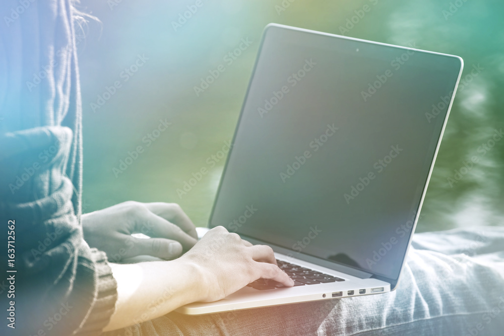 Fototapeta premium girls hands holding laptop in sunlight on natural summer water background