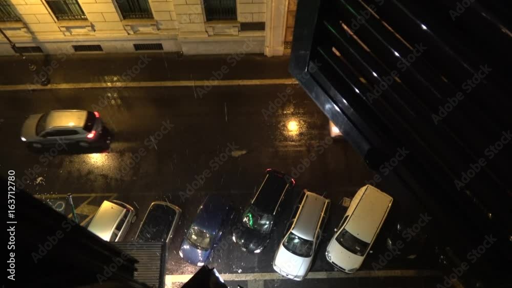 Looking down out of an apartment window showing rainy streets car driving backwards out of parking space carefully first braking for antother car and then driving away to the left bad weather scene 4k