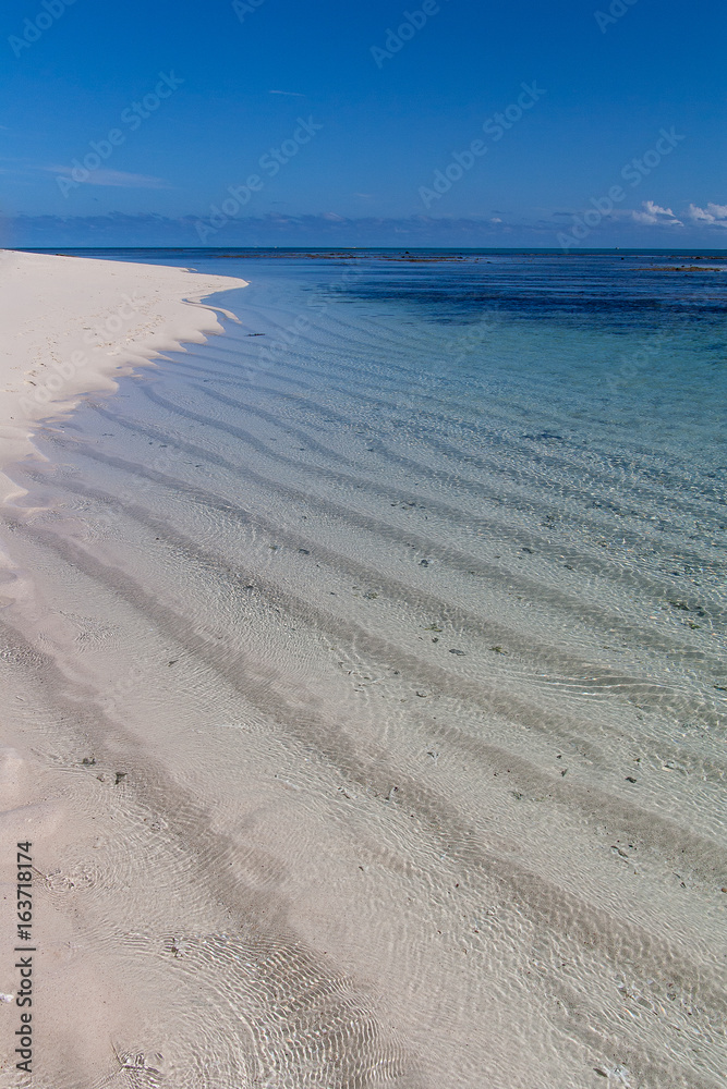 Rippled sand seen through clear, calm water on a clear sunny day in New Caledonia.