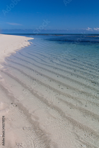 Rippled sand seen through clear  calm water on a clear sunny day in New Caledonia.