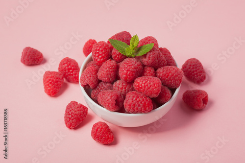 Bowl with fresh raspberries and mint leaves on a pink background. Minimal concept