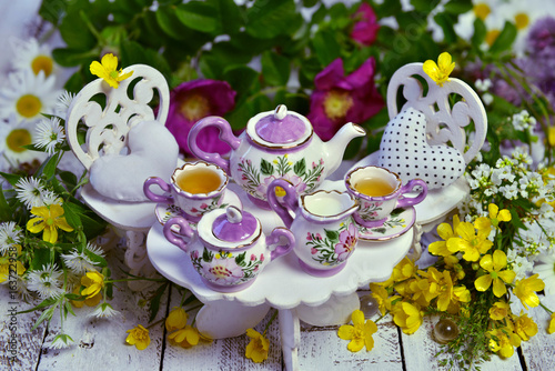 Mad tea party concept with decorated small furniture, cups, teapot and flowers on planks. Alice in Wonderland background photo