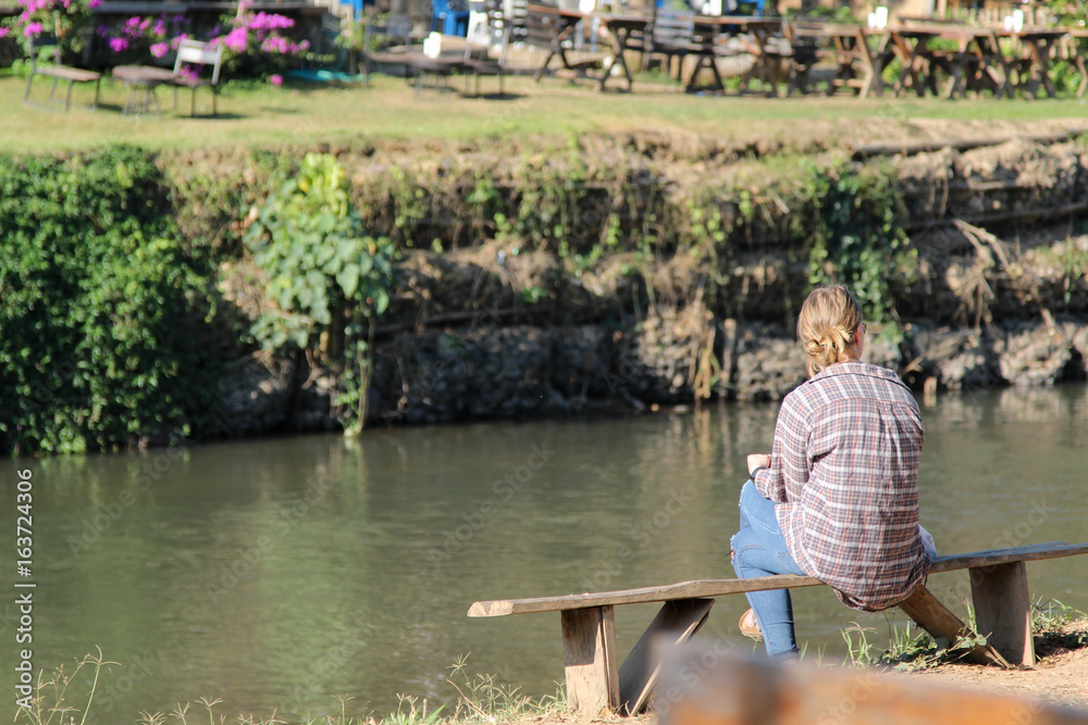 Fototapeta premium Lonely woman sitting on wooden bench at the riverside.