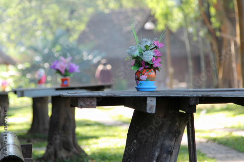 Rose artificial flower in the pot on wooden table in front of cottage resort.